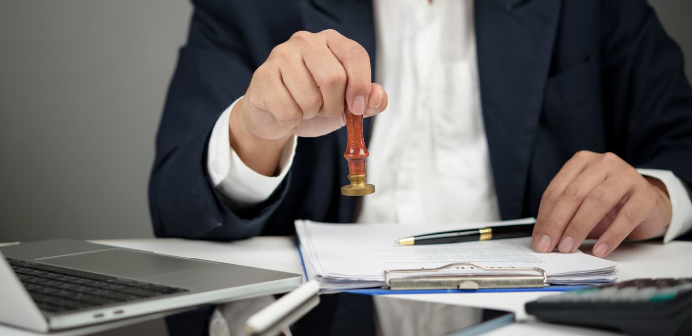 Close-up of a professional stamping documents at a desk with paperwork, pen and laptop visible