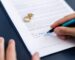 someone signing divorce papers with wedding rings on the paper