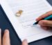 someone signing divorce papers with wedding rings on the paper