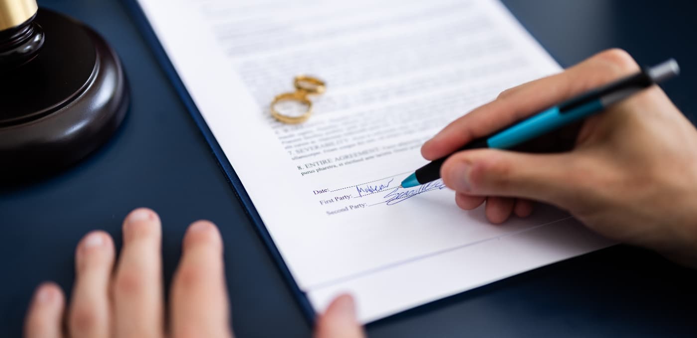 someone signing divorce papers with wedding rings on the paper