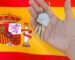 Hand holding house keys with a keyring shaped like a home, set against the Spanish flag.